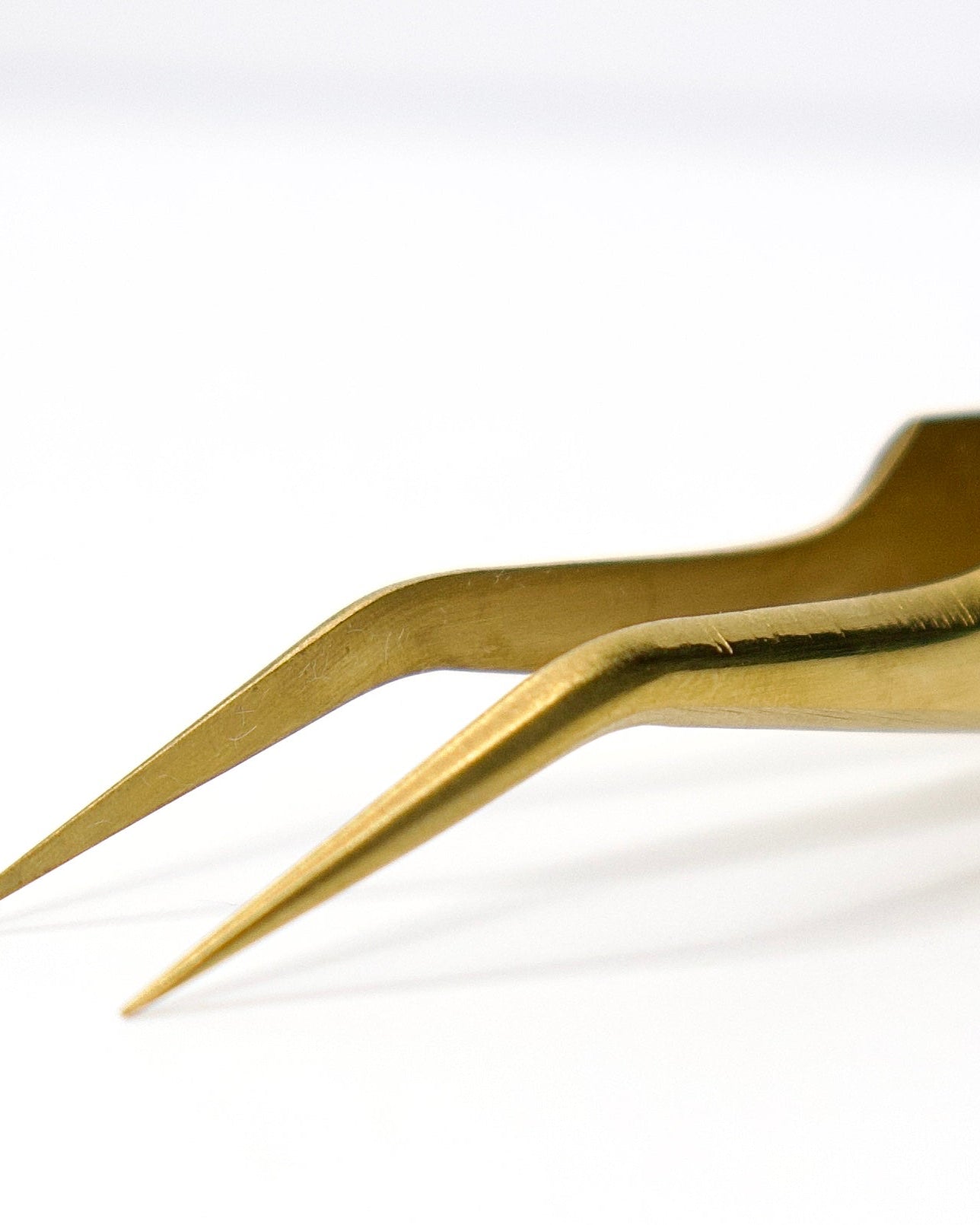 Close-up of a pair of metallic tweezers with a polished gold finish, positioned diagonally on a clean white background.